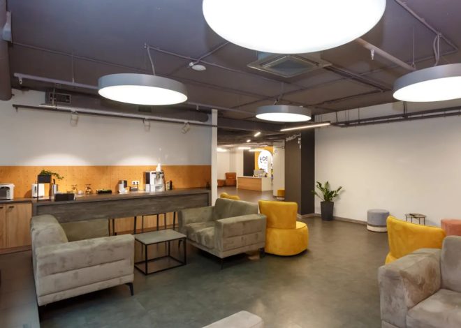 Modern lounge area with gray sofas, yellow chairs, and a coffee bar along a wooden counter.