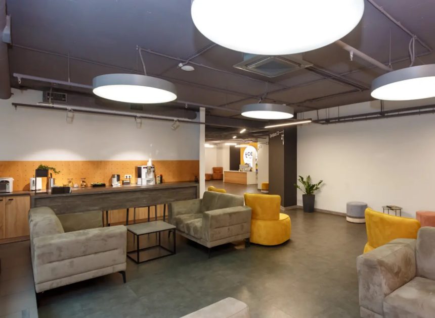 Modern lounge area with gray sofas, yellow chairs, and a coffee bar along a wooden counter.