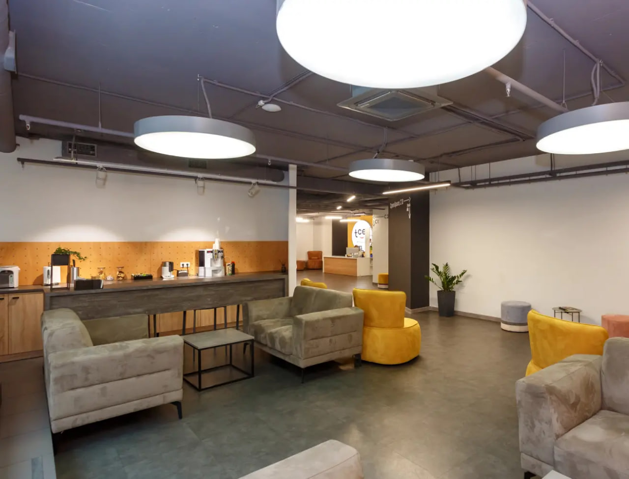 Modern lounge area with gray sofas, yellow chairs, and a coffee bar along a wooden counter.