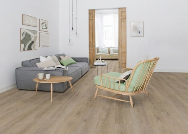 Cozy, minimalist living room with a gray sofa, green cushions, a round wooden coffee table, and a matching wood-framed chair in a bright space with art on the wall.