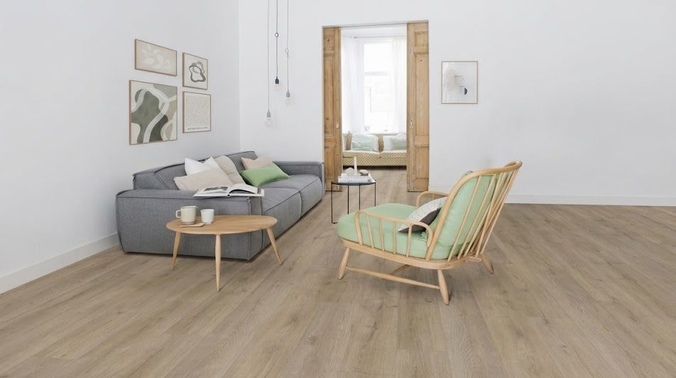 Cozy, minimalist living room with a gray sofa, green cushions, a round wooden coffee table, and a matching wood-framed chair in a bright space with art on the wall.