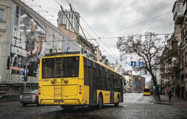 Back view of a yellow trolleybus on a cobblestone street beneath overhead power lines in a city.
