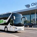 White coach bus with PAN-BUS.net branding parked in front of Chisinau Airport terminal; departures sign visible.